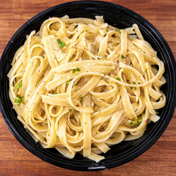 Fettuccine Alfredo pasta with black pepper and parsley in a black bowl on a wooden table.