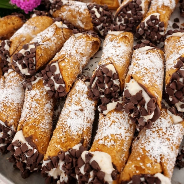 Close-up of cannolis filled with cream, chocolate chips, and dusted with powdered sugar.