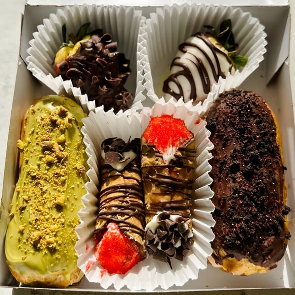 A box of assorted pastries, including chocolate-covered strawberries, cannolis, and eclairs.
