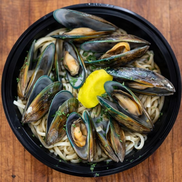 Mussels and pasta with a lemon wedge and parsley in a black bowl on a wooden table.