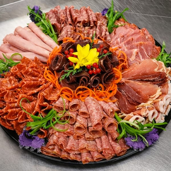 A large charcuterie board filled with various meats, garnished with carrots, berries, and purple flowers.